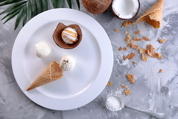 Fototapeta na wymiar Plate with composition of ice cream balls in waffle cone and coconut shell on table