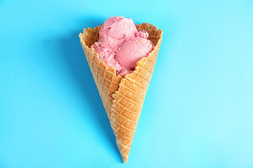 Delicious fruit ice cream in waffle cone on color background