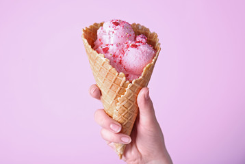 Female hand holding ice cream in waffle cone against pink background
