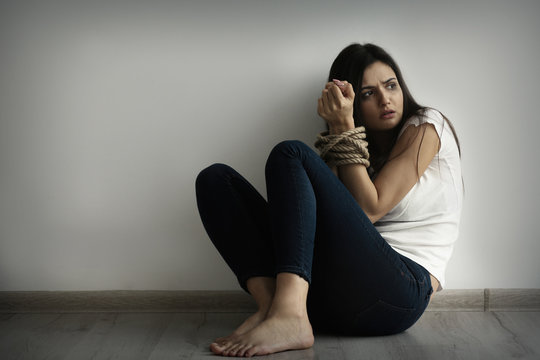 Woman with tied hands sitting on floor against light wall