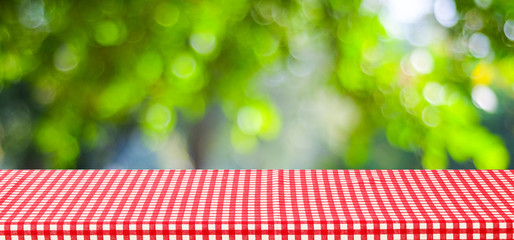 Empty table with red tablecloth over blur green tree and bokeh background, for food and product...