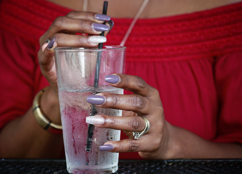 Close up of African American women's hands with beautiful manicure holding  glass with ice water