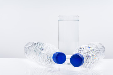 Plastic bottle and glass of mineral water on white background.
