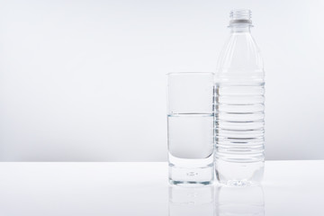 Plastic bottle and glass of mineral water on white background.