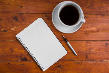 Top view of cup of coffee on table with notebook and pen.