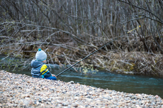Little baby boy is fishing on the bank of a mountain river with a fishing rod in his hands