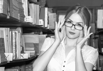 GIRL IN THE LIBRARY BETWEEN racks with books, a beautiful blonde with glasses gets knowledge and education