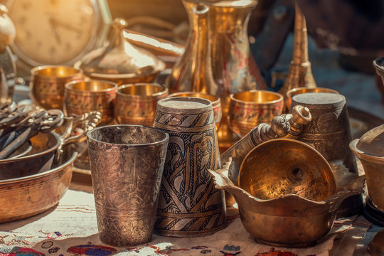 Old Copper Metal Glasses And Pitcher On Counter In Sunday Flea Market. Antique Bazaar