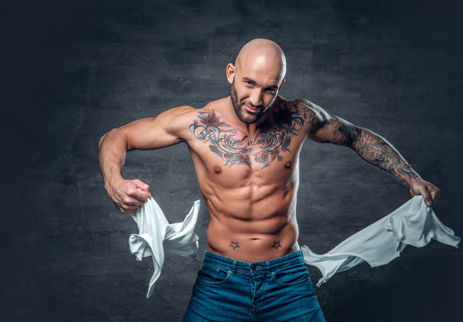 Studio portrait of athletic male with a tattoo on his chest ripping t shirt.