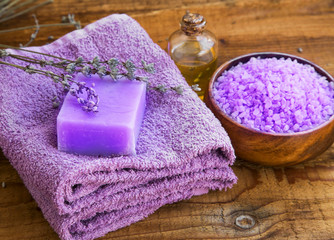 Obraz na płótnie Canvas Lavender flowers extract spa soap, oil bottle and bath salt bowl on wooden board with soft purple towels