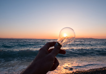 Man holding light bulb against sun on beach
