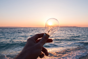 Man holding light bulb near sea at sunset