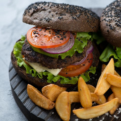 Close-up of black beef burger with potato wedges, selective focus, studio shot