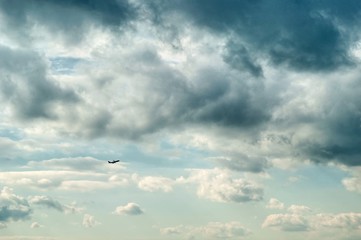 Unique beautiful dramatic gray and white clouds on light blue sky on daylight. The silhouette of airplane rising upward the clouds after takeoff. Air travel concept.