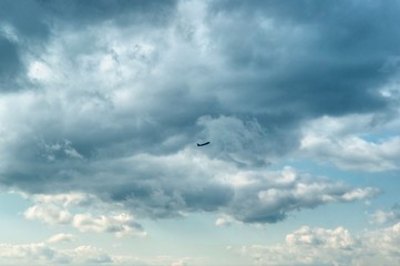 Unique beautiful dramatic gray and white clouds on light blue sky on daylight. The silhouette of airplane rising upward the clouds after takeoff. Air travel concept.