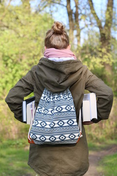 teenager girl holds many books walking on path