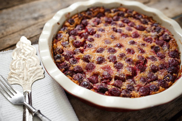 Cherry clafoutis pie in ceramic baking pan with spatula on wooden board