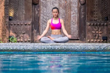Fototapeten Asia woman doing yoga beside swimming pool © Peera