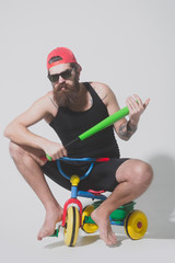 bearded angry man holds green baseball bat on bicycle toy