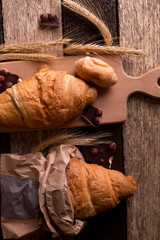 Croissants with chocolate on board near wheat on wooden sackcloth background. Rustic style. Top view.
