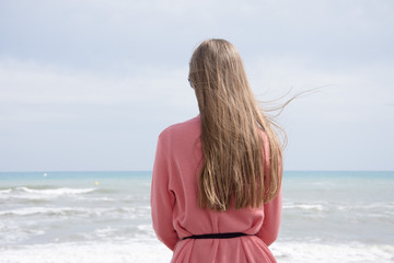 Obraz premium A lonely girl sitting on a bench by the sea and looking at the storm sea