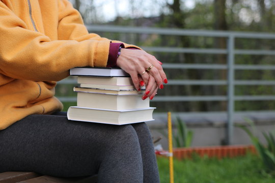 Kobieta siedzi na ławce w parku z książkami na kolanach