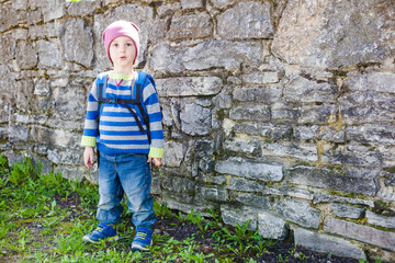 Boy with backpack standing near a stone wall.