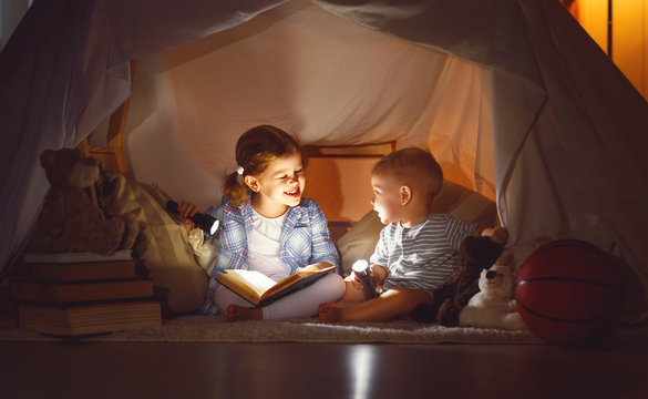 children boy and girl reading book with  flashlight in  tent .