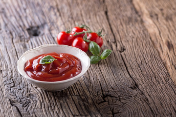Ketchup or tomato sauce in white bowl and cherry tomatoes on wooden table.