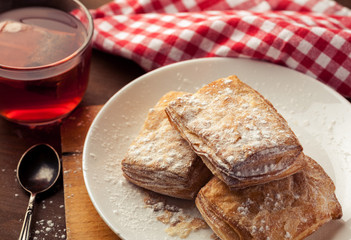 Puff pastries in a white plate with cup of red herbal tea on a wooden table, selective focus