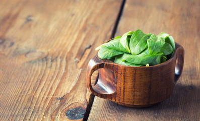 Baby spinach leaves in a bowl on dark wooden background, selective focus..