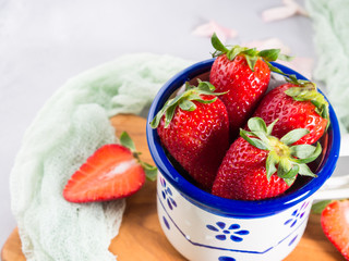 Ripe strawberries in enamel mug on wooden board with textile. Spring summer healthy snack with fruit