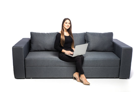 Happy Brunette Woman Sitting On Sofa With Laptop On White Background