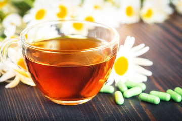 Herbal tea in a transparent cup, capsules and chamomile flowers on wooden table. The concept of phytotherapy.