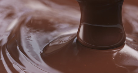 Slow motion of premium dark melted chocolate being poured from spoon in right part of frame, 4k photo