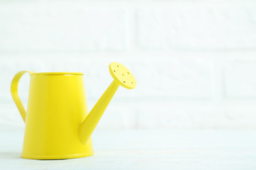 Yellow watering can on the brick wall background