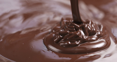 Slow motion of premium dark melted chocolate being poured from spoon in right part of frame, 4k photo