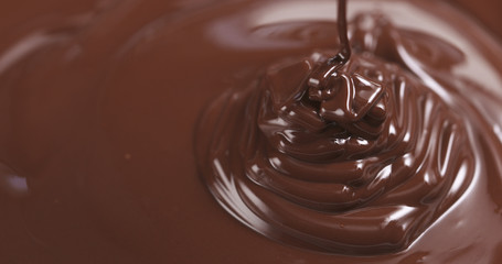 Slow motion of premium dark melted chocolate being poured from spoon in right part of frame, 4k photo
