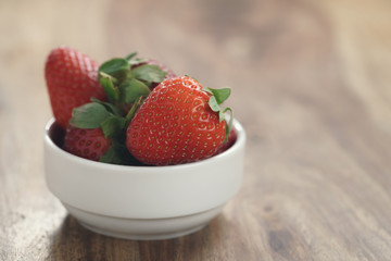ripe organic strawberries in white bowl on wood table, with copy space