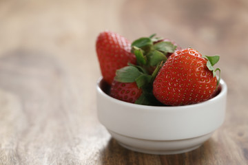 ripe organic strawberries in white bowl on wood table, with copy space