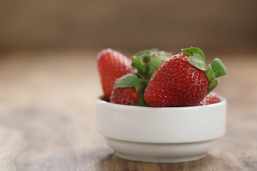 ripe organic strawberries in white bowl on wood table, with copy space