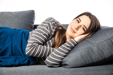 Fototapeta premium Young woman lying on sofa covered by plaid and look at camera on white