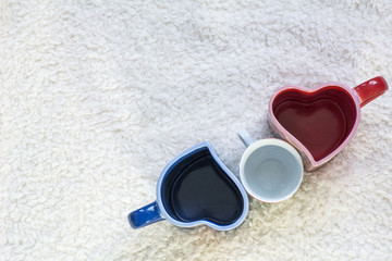 Blue and red cups in form of heart and white small one on the white fur background