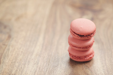 closeup shot stack of pastel colored macarons with strawberry flavour on wood table, vintage toned...
