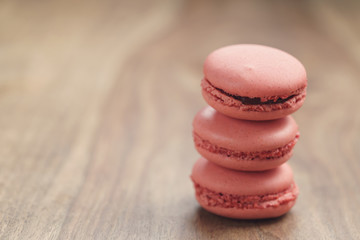 Fototapeta na wymiar closeup shot stack of pastel colored macarons with strawberry flavour on wood table, vintage toned photo