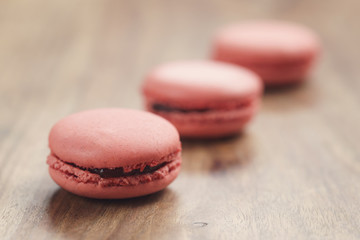 Obraz na płótnie Canvas closeup shot pastel colored macarons with strawberry flavour on wood table, vintage toned photo
