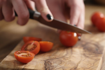 teen girl cuts cherry tomatoes on olive cutting board, shallow focus