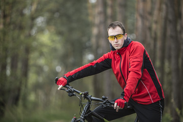 Young attractive man wears red suit on bike in the forest