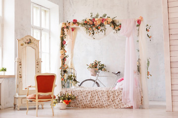 Rustic interior of the bedroom. A bed with an arch of flowers, a mirror, an armchair and a retro bicycle stands at the wall.