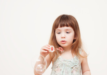 Girl blows soap bubbles on monophonic background